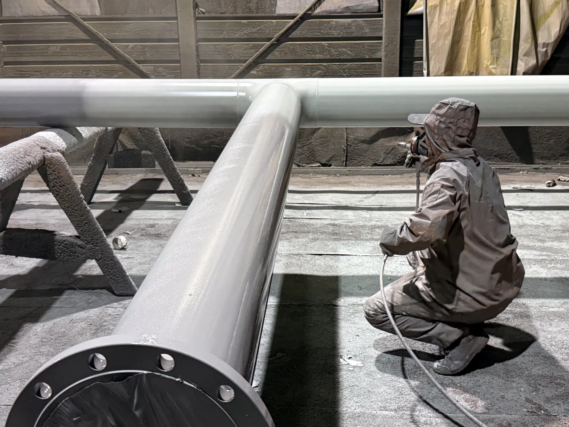 Painter in protective gear spraying a large diameter pipe with a flanged end