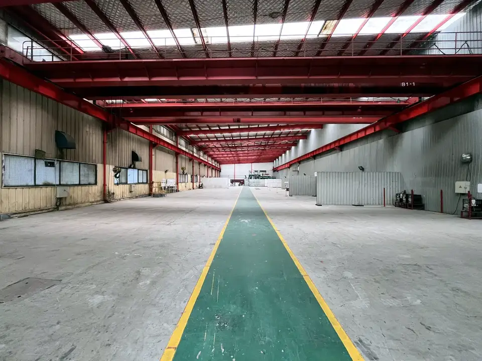 Empty fabrication hall with a green and yellow walkway between red roof girders