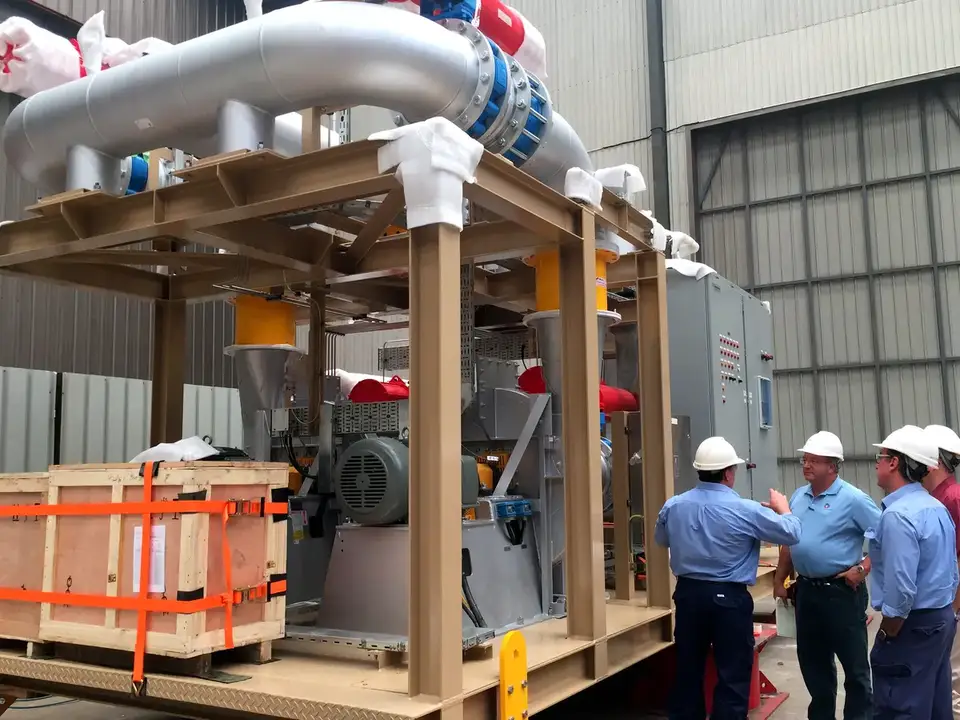 Inspectors in hard hats reviewing a packaged equipment skid with a crated machine
