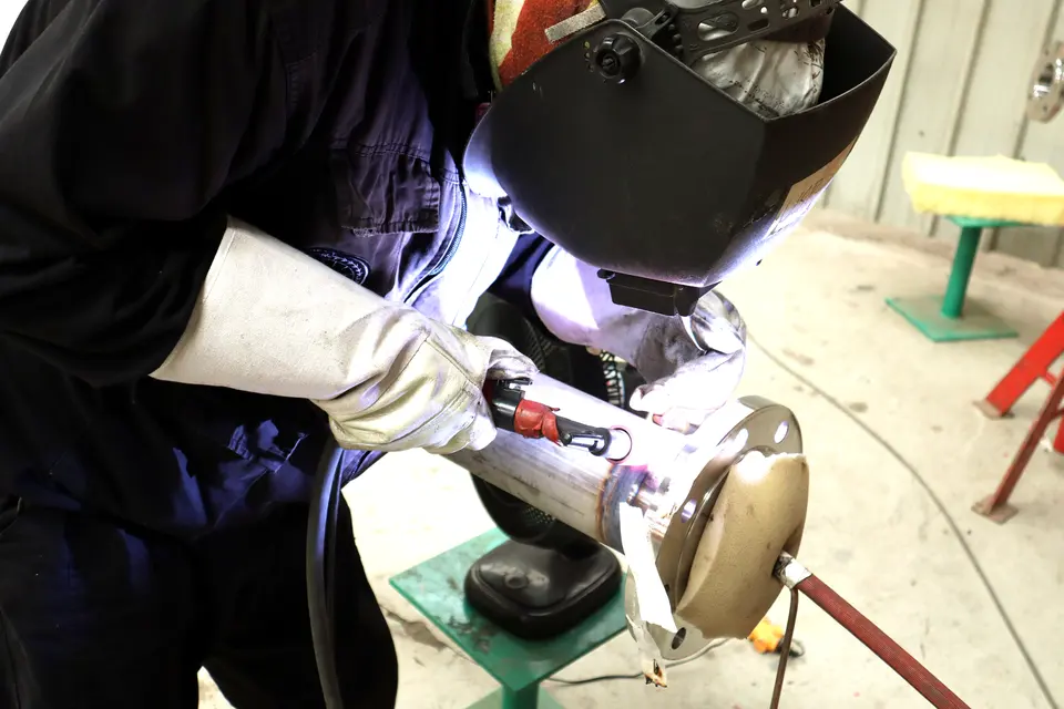 Welder in a helmet welding a stainless pipe to a flange